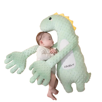 Baby lying on a green dinosaur-shaped pillow with 'LOVELY' text on a beige background.